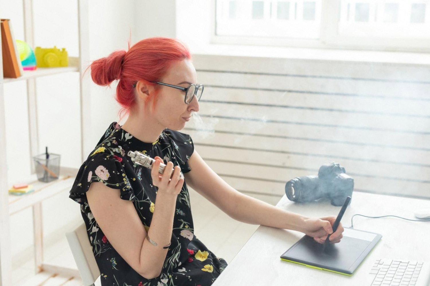 Woman at a bright desk using a disposable vape while working on a tablet